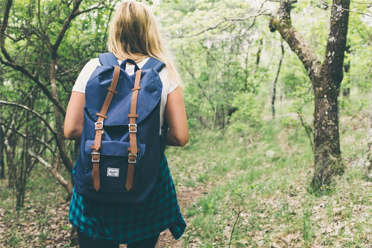junge Frau mit Wanderrucksack auf Waldweg